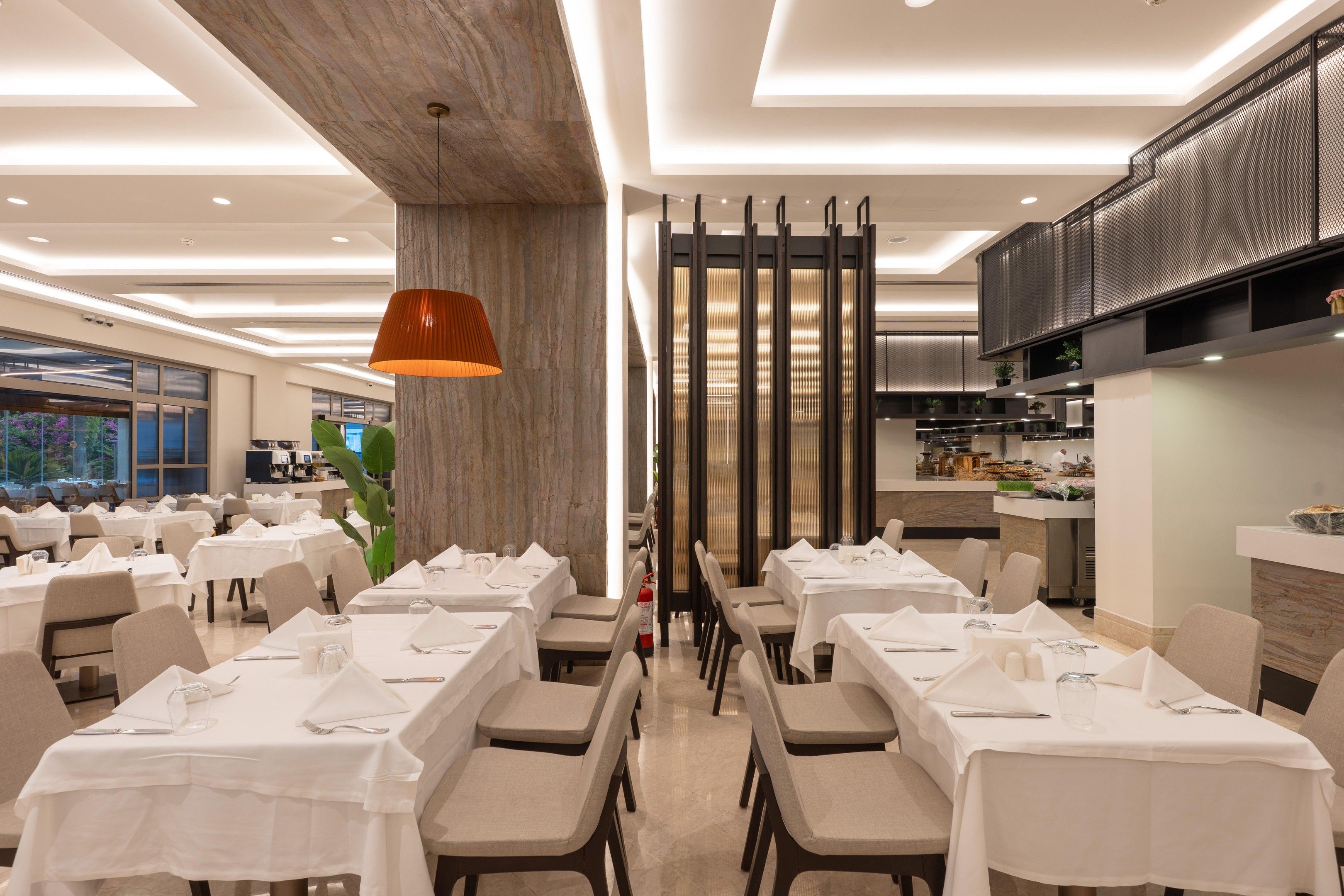 Un restaurant doté de plusieurs tables, d’une colonne centrale et d’un espace cuisine.