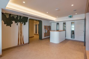 A modern reception area with a central desk, a wall-mounted security camera, and a green exit sign. -  Mirage Park Resort - Premium All Inclusive (Kemer)