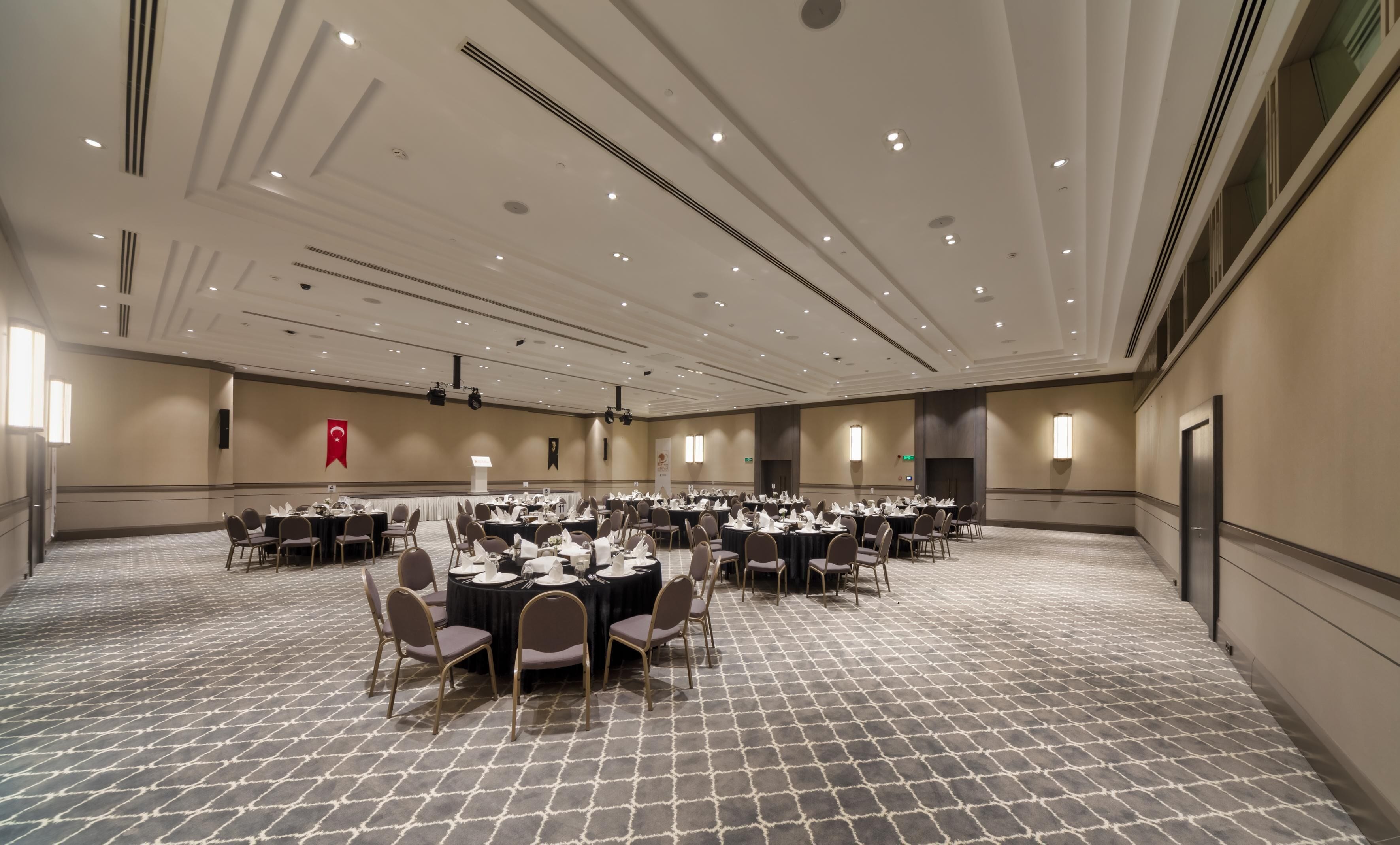 Een ruime congreszaal met meerdere ronde tafels, elk voorzien van stoelen en servies.