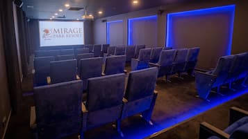 Cine con filas de asientos, una pantalla mostrando 'MIRAGE PARK RESORT' y una luz ambiental azul.