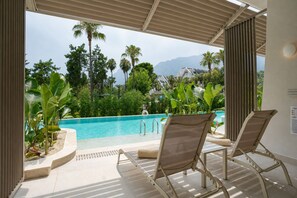 A poolside area with two lounge chairs, a pool, and a view of a mountainous landscape. -  Mirage Park Resort - Premium All Inclusive (Kemer)