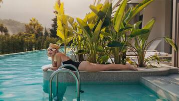 Una persona descansando al lado de una piscina, con vista a un paisaje tropical y un edificio de diseño moderno.