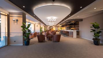 A modern hotel lobby with a bar area, seating, and potted plants.
