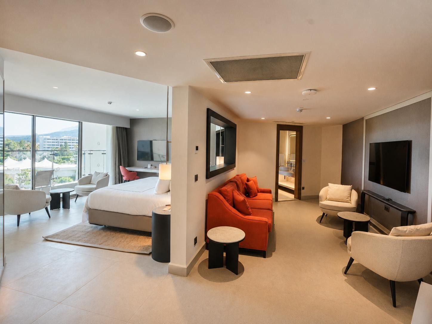 A modern hotel room with a large bed, a sofa, a TV, and a balcony with a view.