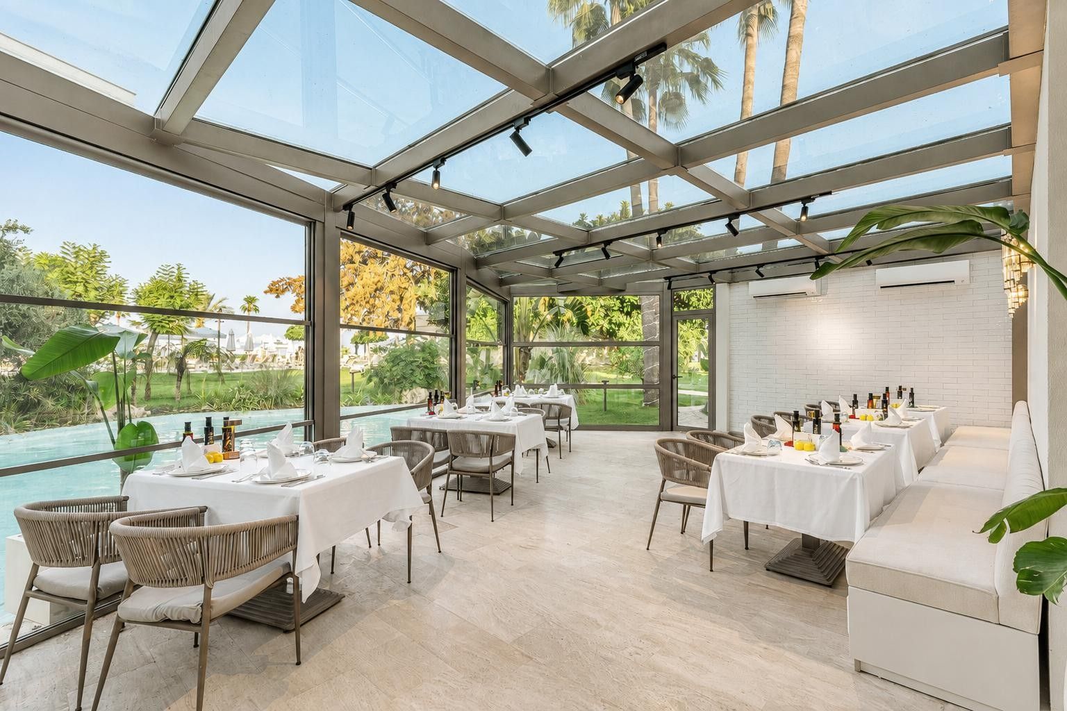 A restaurant with a glass ceiling, outdoor views, and a pool.