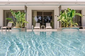 Une piscine avec des chaises longues et des plantes en pot.