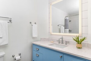 A modern bathroom with a marble sink, a large mirror, and a blue cabinet.