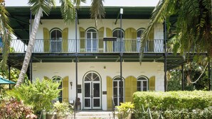Un edificio de dos plantas con balcón, ventanas arqueadas y techo verde.