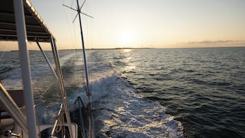 A boat's deck with a view of the ocean and a distant shoreline at sunset.