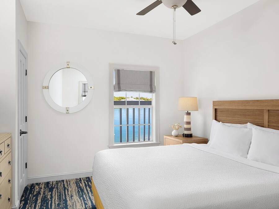 Habitación de hotel con una cama, un televisor sobre una cómoda, un espejo redondo, una ventana con vistas y un ventilador de techo.