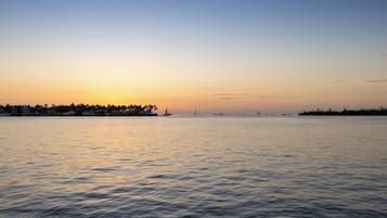 Una orilla tranquila al atardecer, con veleros y una costa lejana.