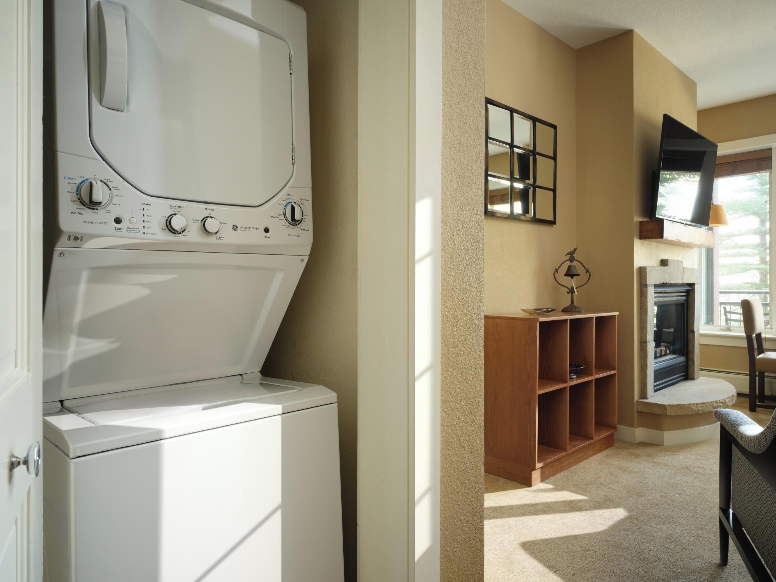 A laundry room with a washer and dryer, a wooden shelf, a fireplace, and a television mounted on the wall.