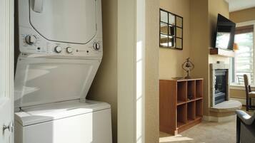 A laundry room with a washer and dryer, a wooden shelf, a fireplace, and a television mounted on the wall.