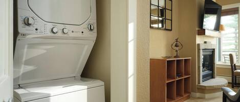 A laundry room with a washer and dryer, a wooden shelf, a fireplace, and a television mounted on the wall.