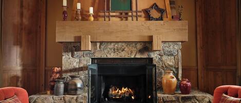 A cozy room with a stone fireplace, a wooden mantel, and two red armchairs.