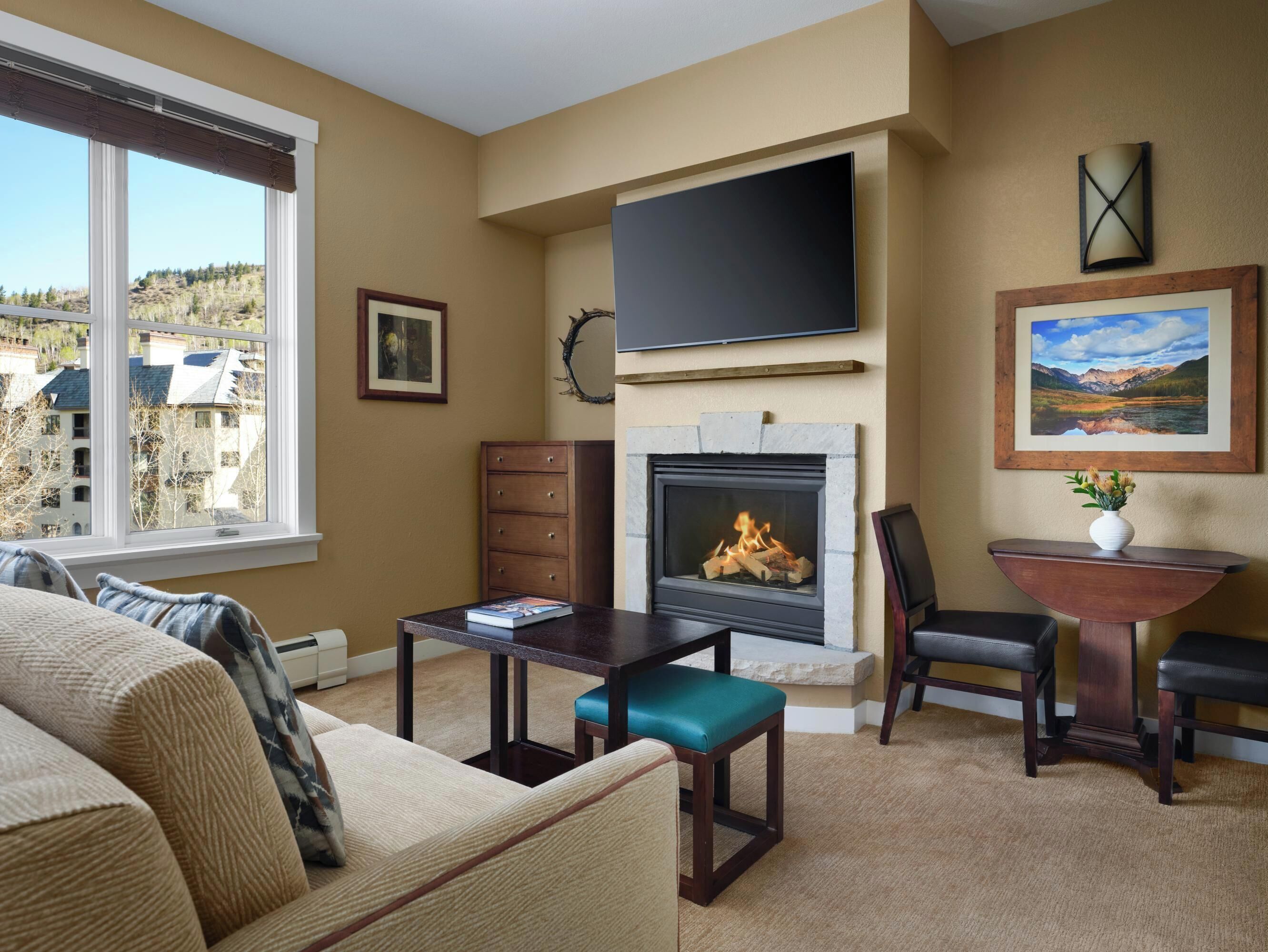 A living room with a fireplace, a flat-screen TV, and a view of a mountainous landscape through large windows.