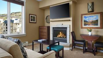 Un salón con chimenea, un televisor de pantalla plana y vistas a un paisaje montañoso a través de amplios ventanales.