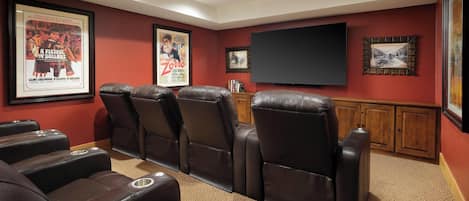 A home theater with reclining leather chairs, a large flat-screen TV, and framed movie posters on the walls.