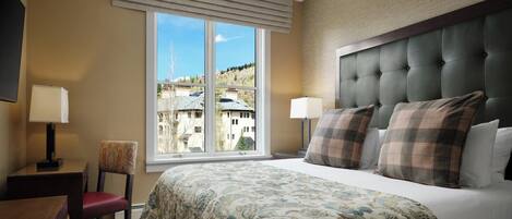 Habitación de hotel con una cama grande, dos lámparas de noche, una silla, un escritorio y una ventana con vistas a edificios.