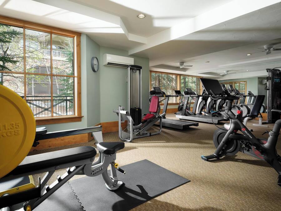 Ein Fitnessraum mit Trainingsgeräten, großen Fenstern und einem Deckenventilator.