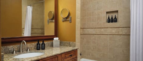 A bathroom with a granite countertop, wooden cabinets, a white sink, a mirror, a bathtub, and a shower curtain.