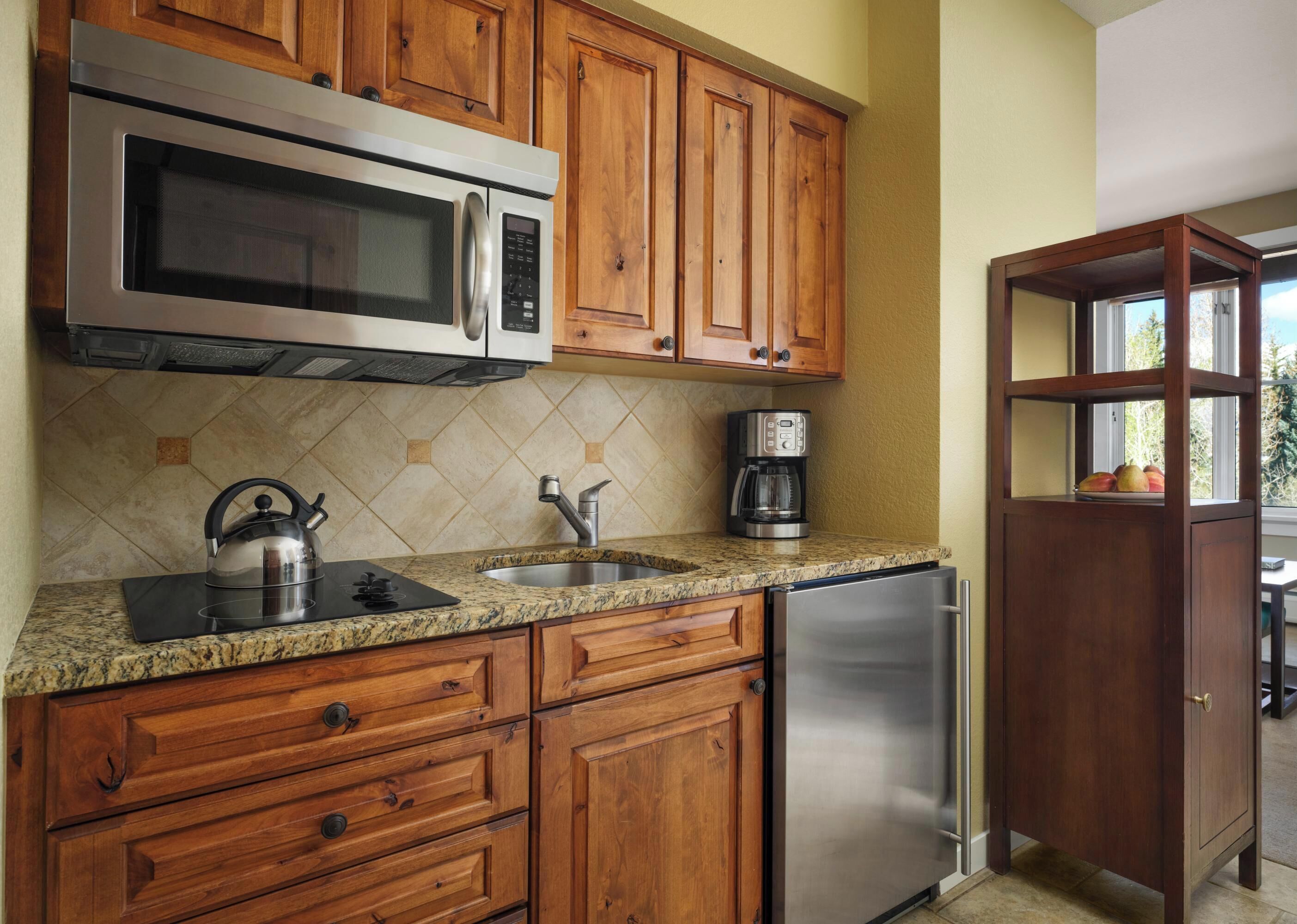 A kitchen with wooden cabinets, a stainless steel refrigerator, a microwave, a kettle, and a coffee maker.