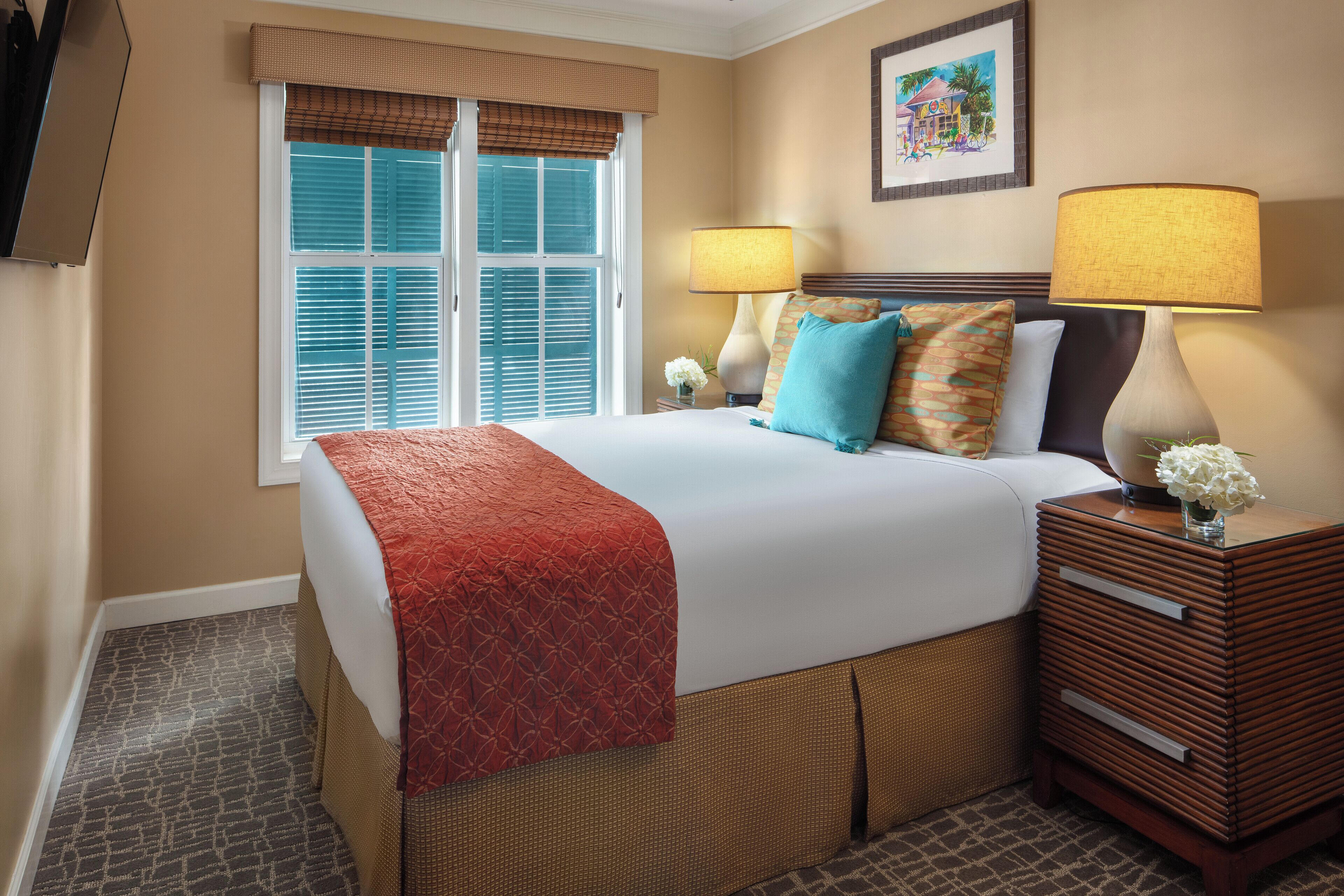 A hotel room with a large bed, two bedside lamps, a nightstand, and a window with blinds.