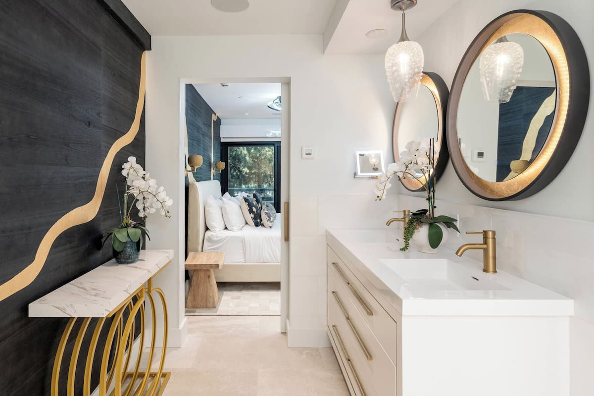 A modern bathroom with a white vanity, gold fixtures, and a large mirror.