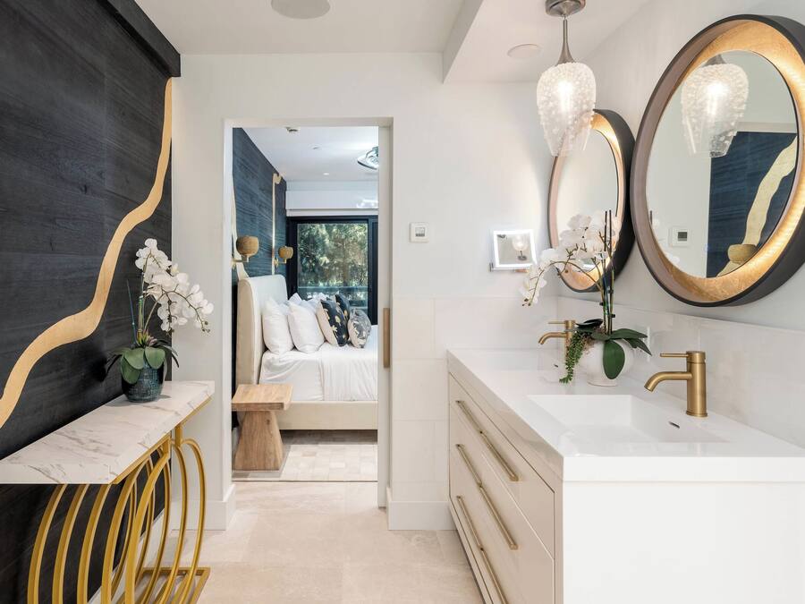 A modern bathroom with a white vanity, gold fixtures, and a large mirror.