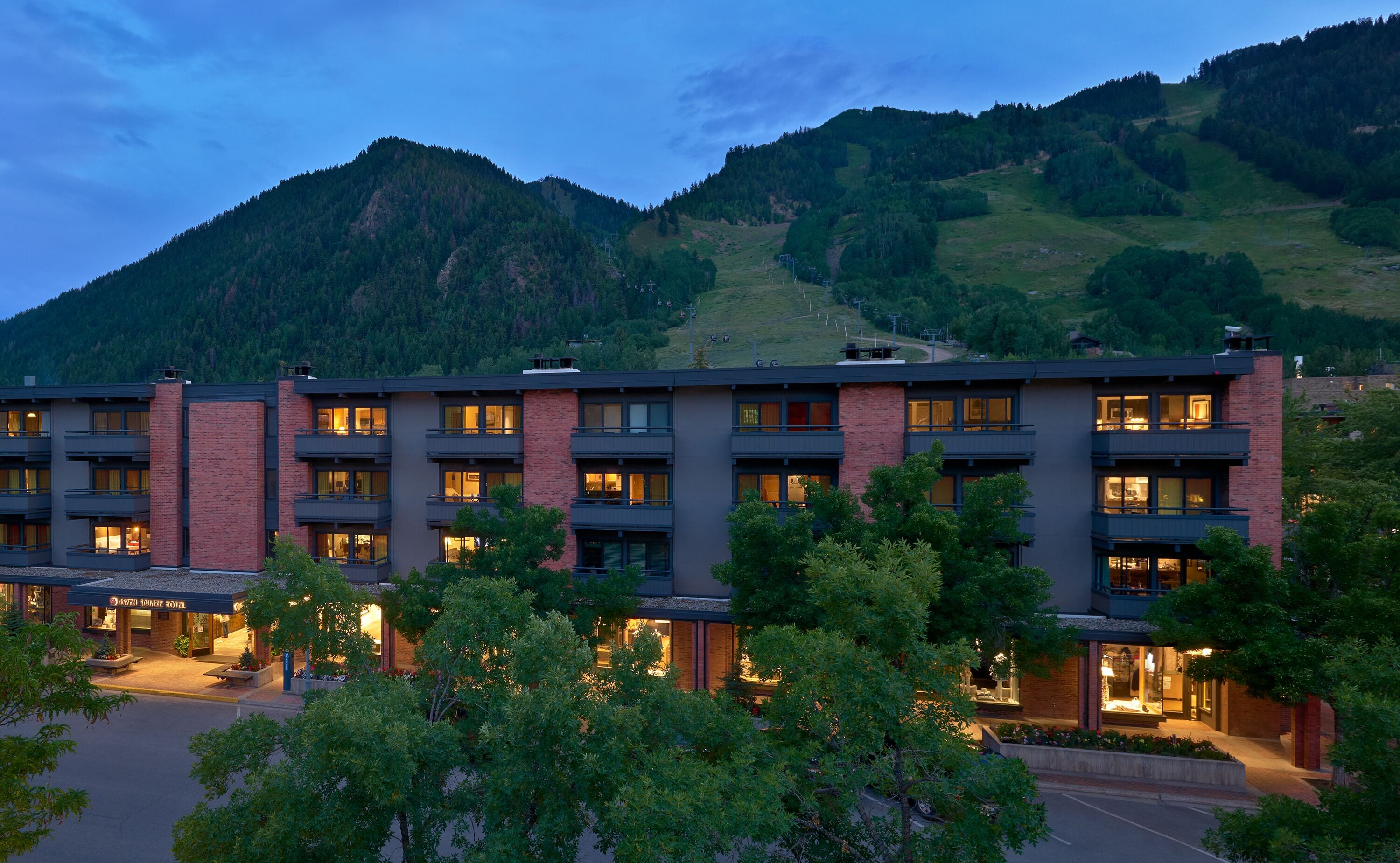 A multi-story hotel with a modern design, featuring balconies and large windows. The hotel is situated in a mountainous area with a view of the surrounding landscape.