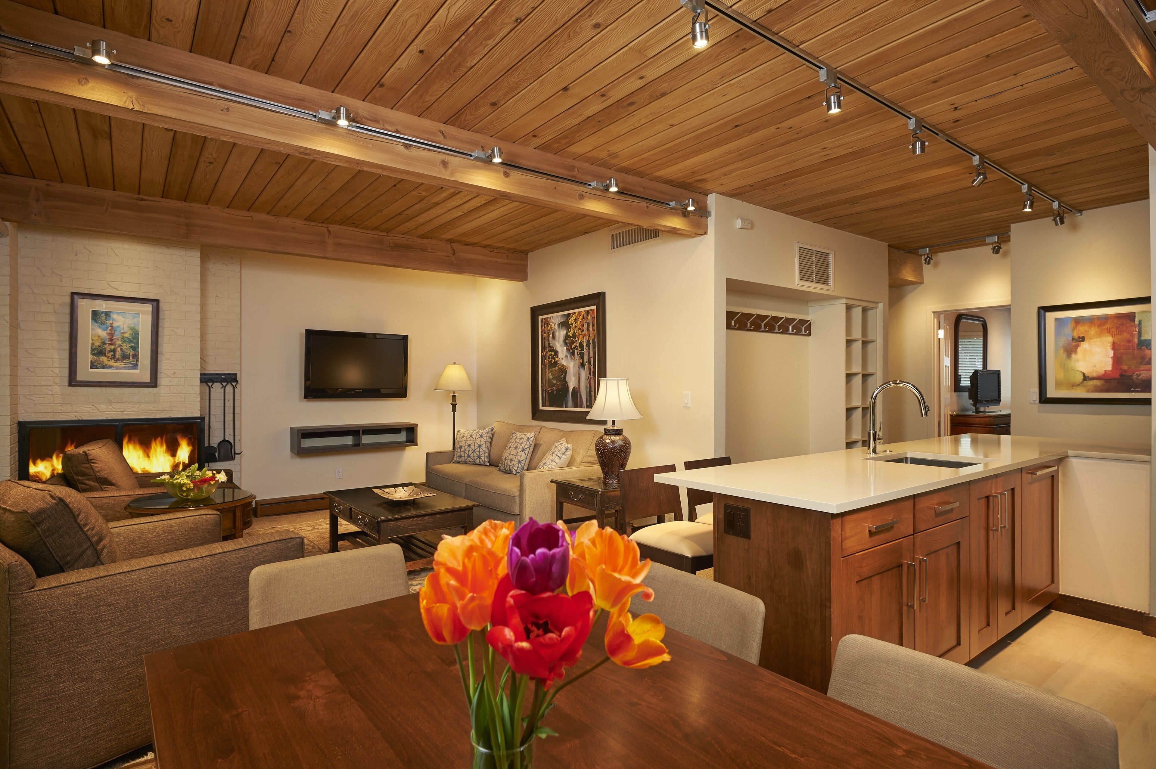 A modern living room with a fireplace, a dining area with a wooden table, and a kitchen with a white countertop.
