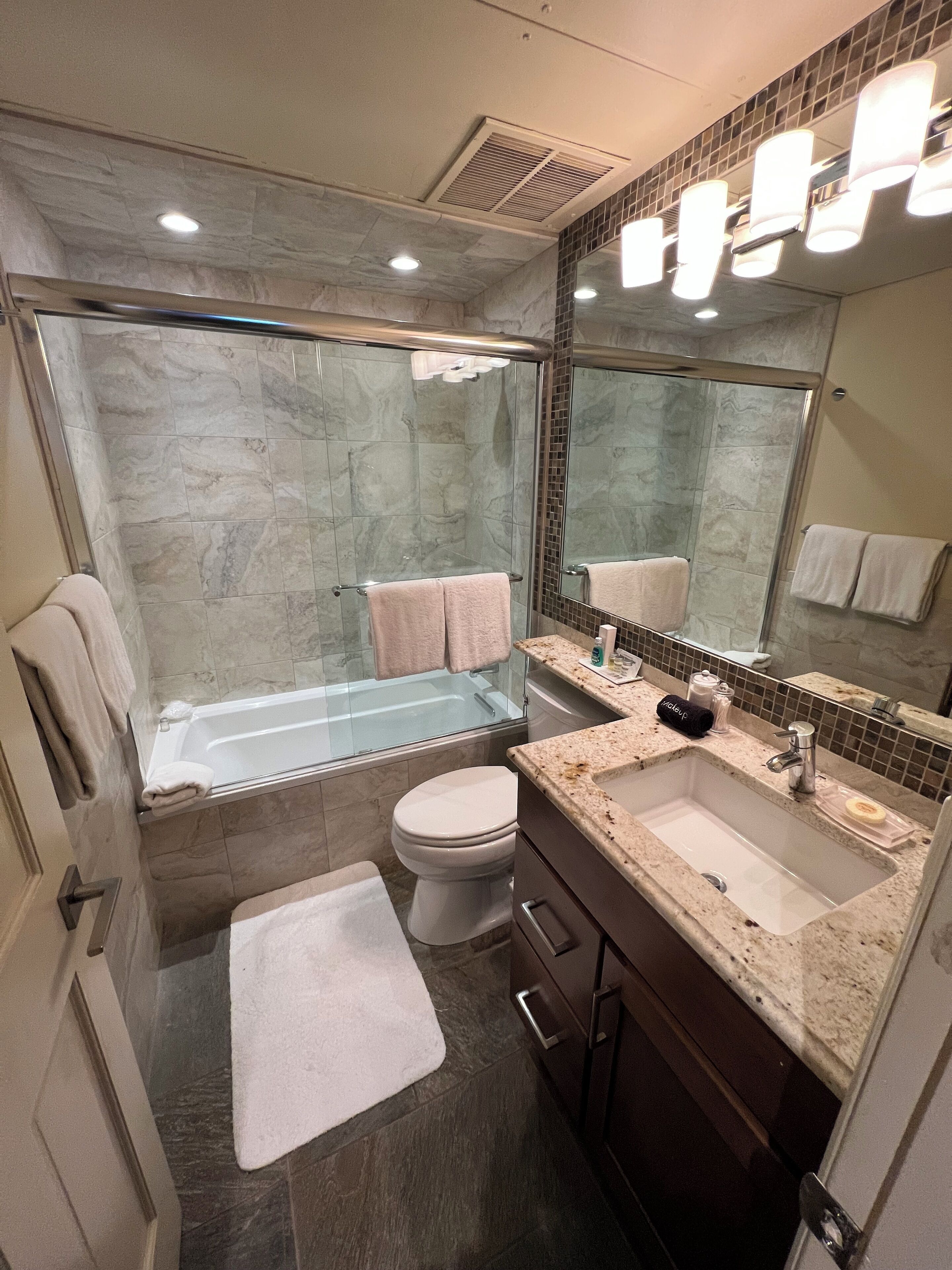 A modern bathroom with a glass-enclosed shower, a bathtub, a toilet, and a vanity with a sink.