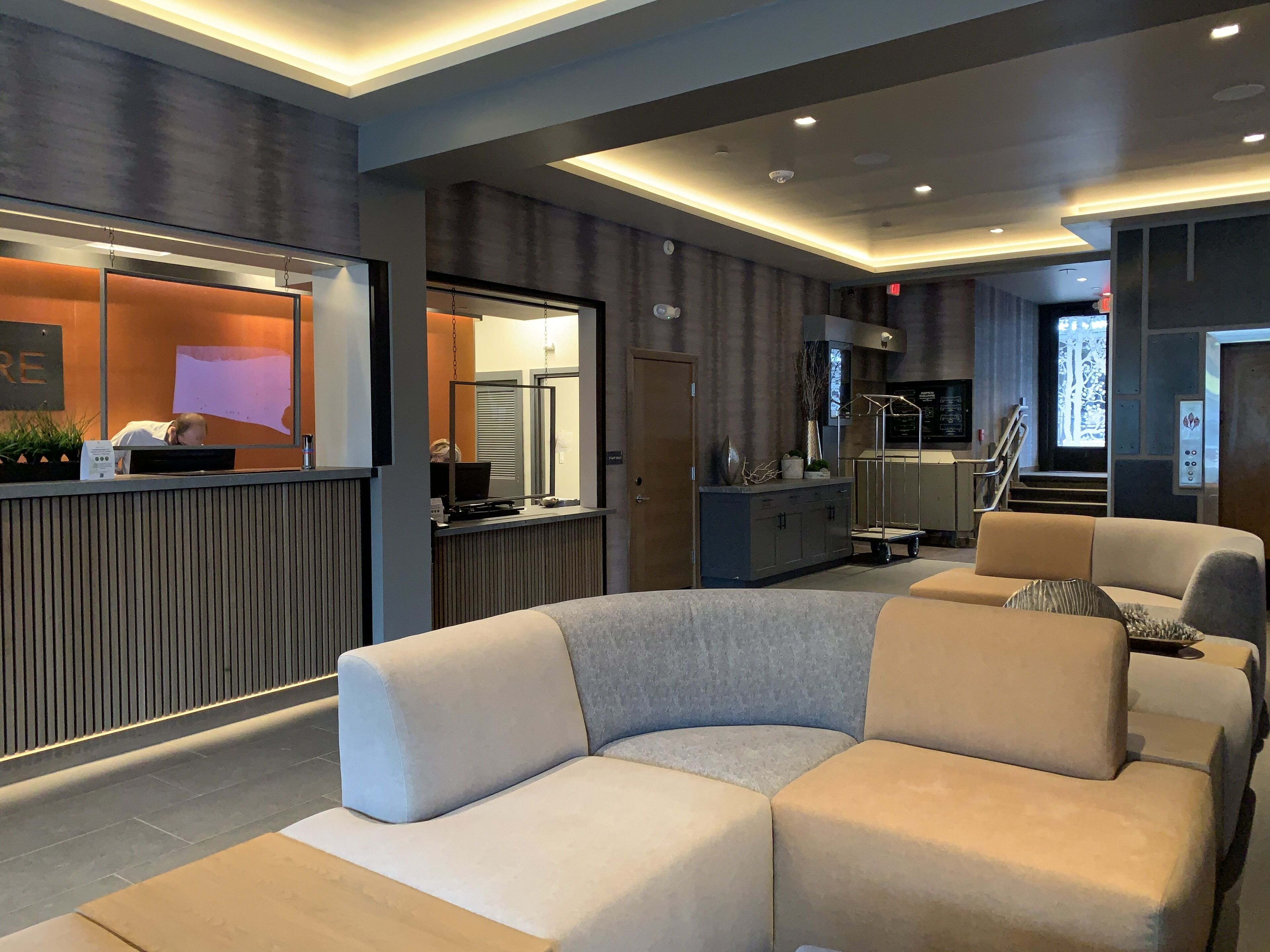 Un moderno vestíbulo de hotel con mostrador de recepción, área de descanso y una escalera que conduce a los pisos superiores.