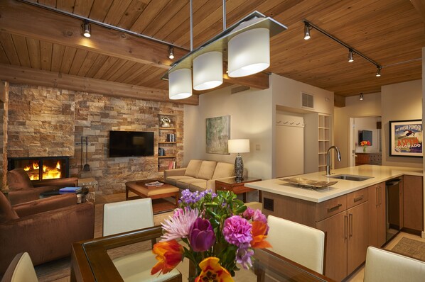 A modern living room with a stone fireplace, a flat-screen TV, and a dining area with a wooden island. - Aspen Square Condominium Hotel (Aspen)