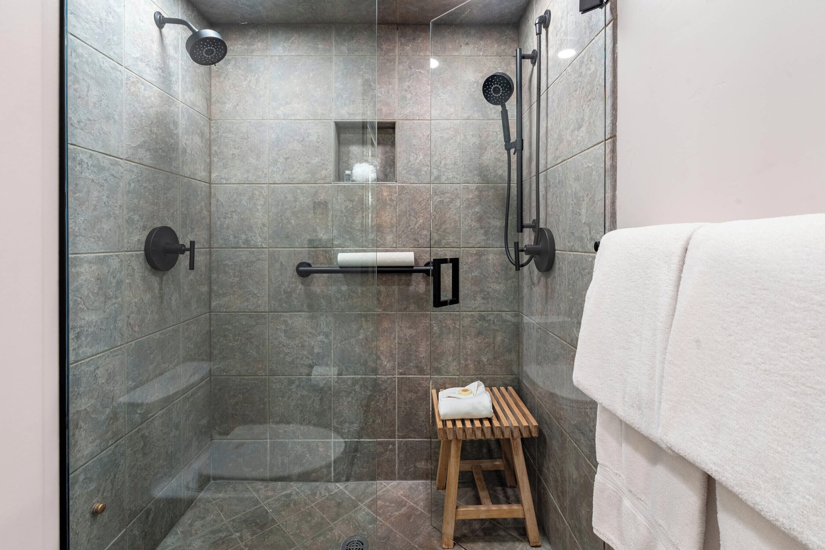 Une douche moderne avec une porte en verre, un tabouret en bois et un porte-serviettes.