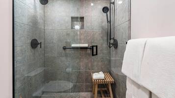 Une douche moderne avec une porte en verre, un tabouret en bois et un porte-serviettes.