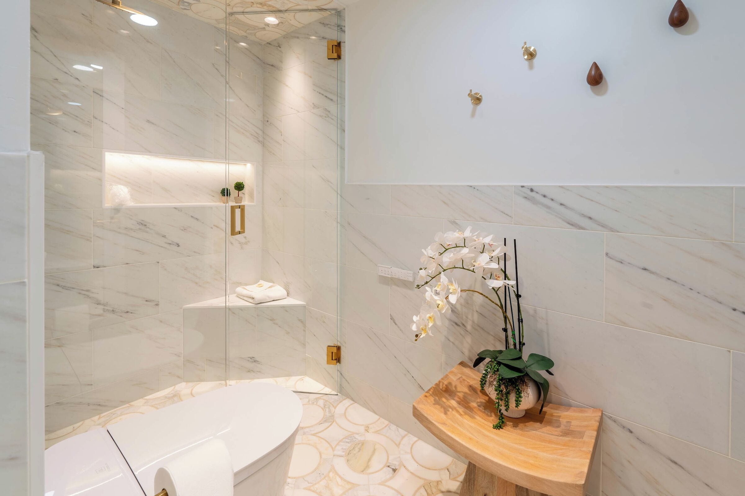 Une salle de bain moderne avec une douche à parois de verre, une baignoire blanche et un meuble-lavabo en bois agrémenté d’une orchidée en pot.