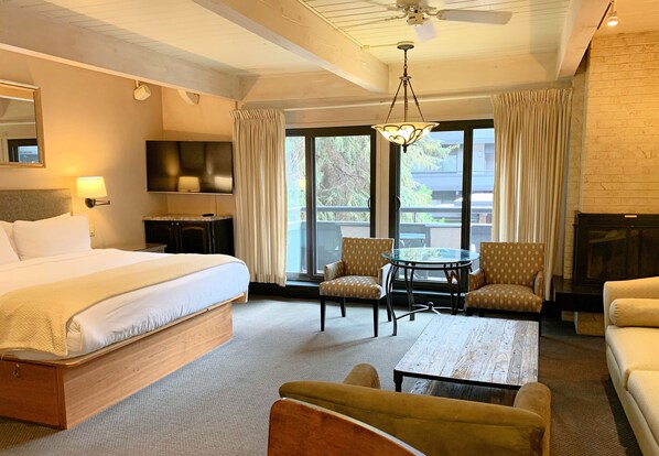 Habitación de hotel con cama, dos sillones, una mesa de centro, televisor y vistas al balcón.