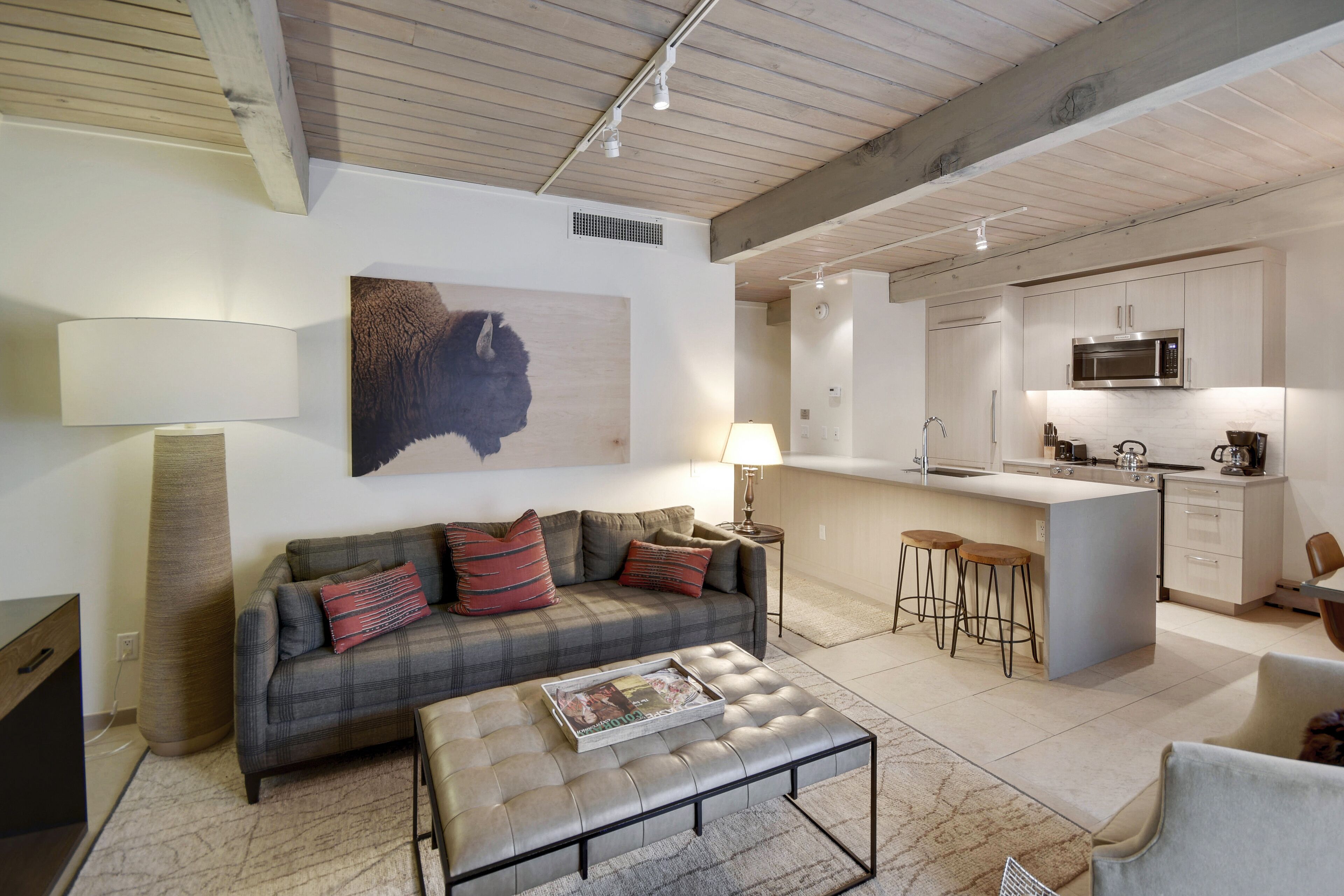 Eine moderne Küche mit einer zentralen Kochinsel, einem Essbereich mit Sofa und Hocker, und einem großen Kunstwerk an der Wand.
