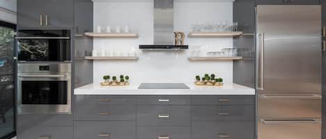 A modern kitchen with grey cabinetry, stainless steel appliances, and decorative plants.