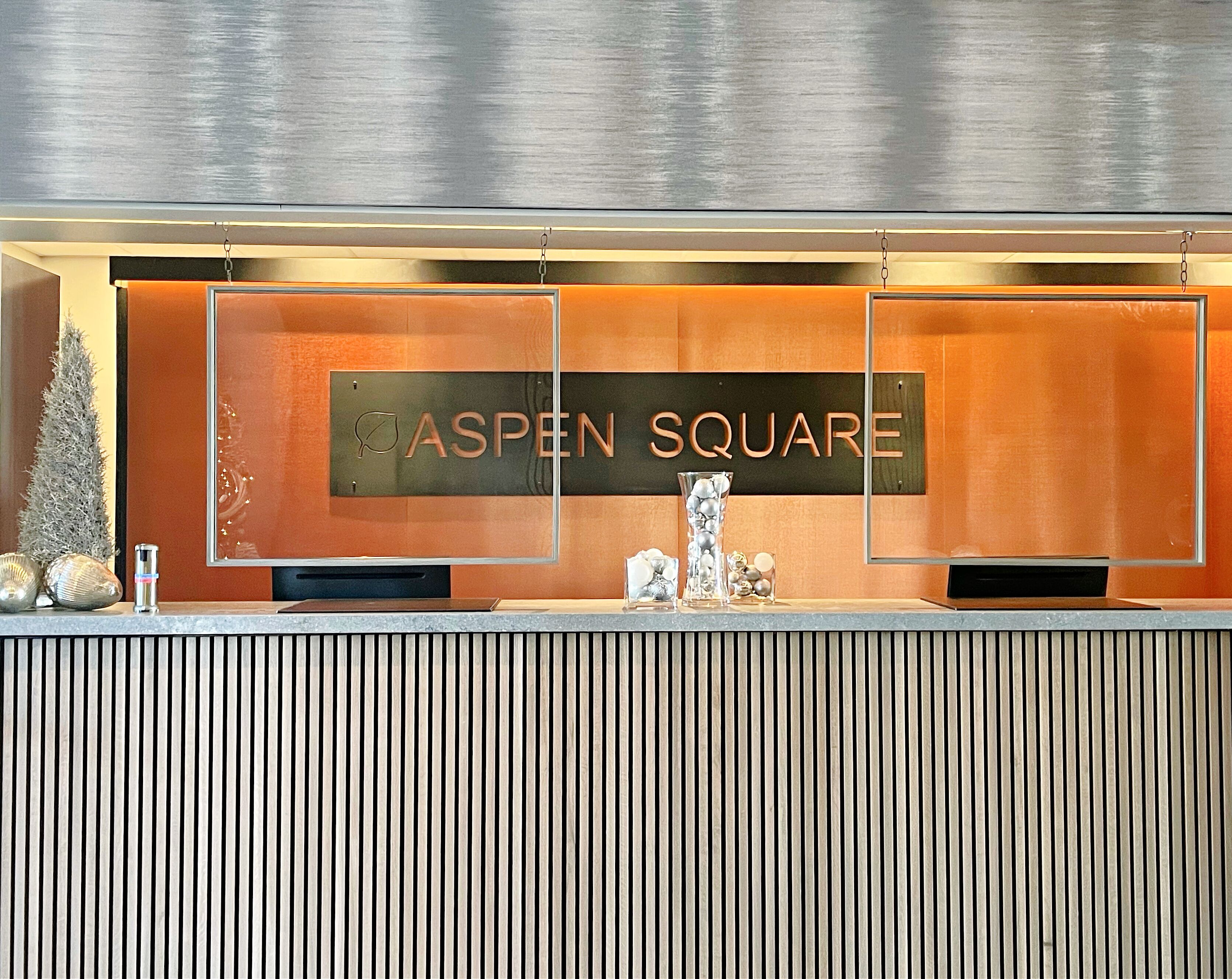 A reception desk with a sign reading "ASPEN SQUARE" and a vertical striped wall behind it.