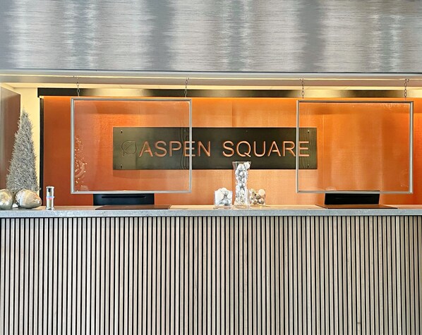A reception desk with a sign reading "ASPEN SQUARE" and a vertical striped wall behind it. - Aspen Square Condominium Hotel (Aspen)