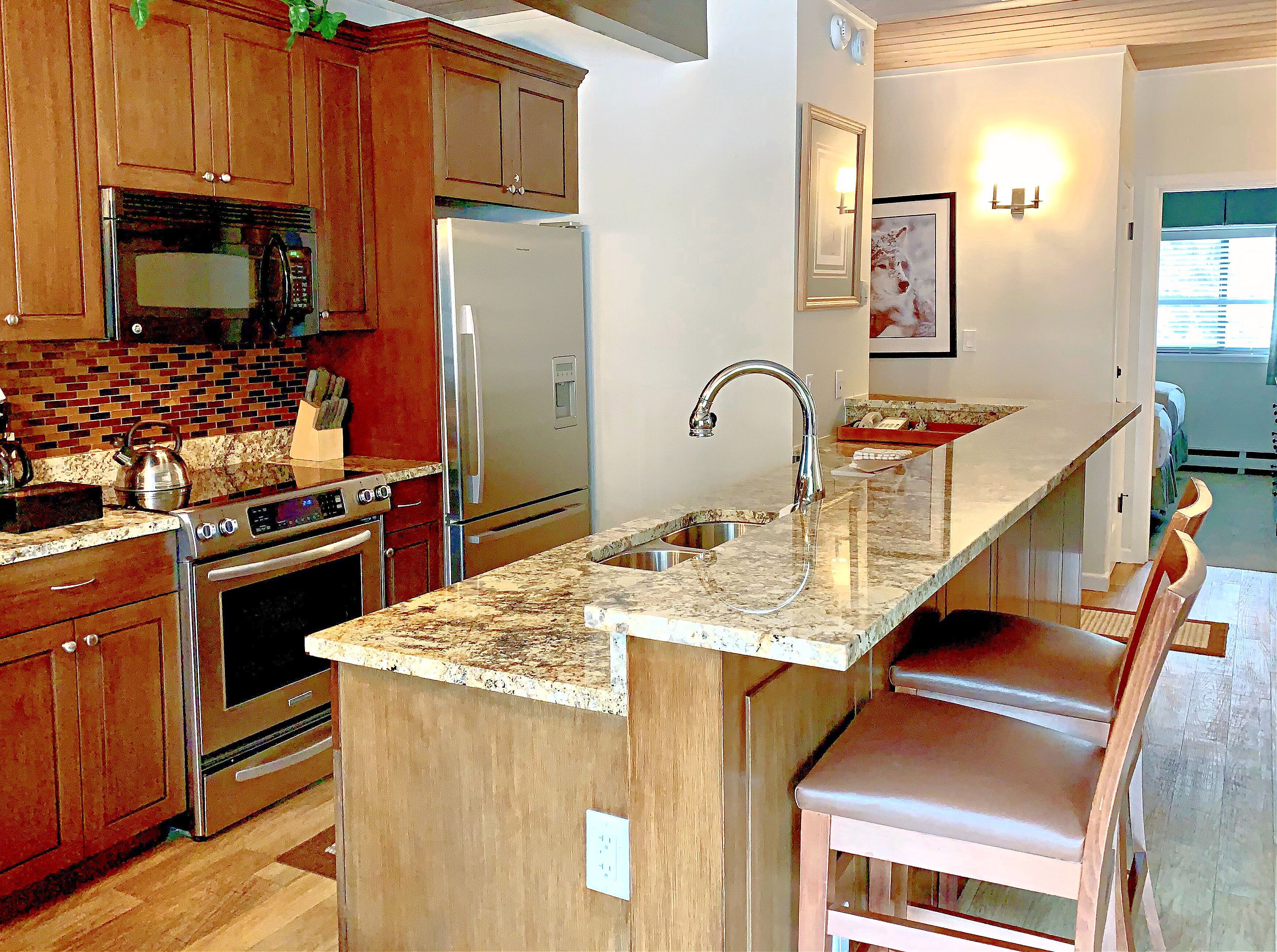 Una cocina con armarios de madera, electrodomésticos de acero inoxidable, encimera de granito y un taburete de bar.