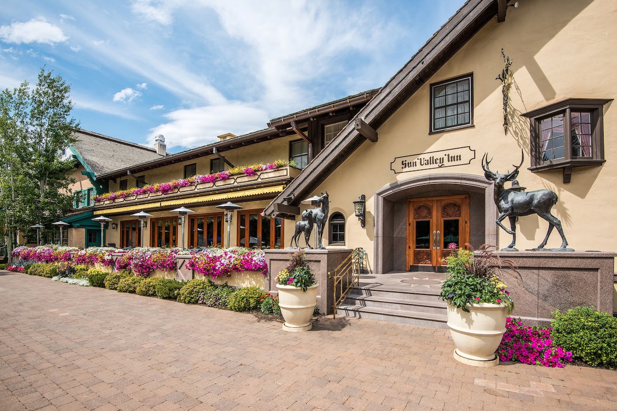A hotel with a sign reading "Sun Valley Inn," featuring a large entrance with steps, a balcony with flower boxes, and a statue of a deer on the facade.