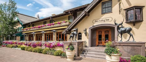 A hotel with a sign reading "Sun Valley Inn," featuring a large entrance with steps, a balcony with flower boxes, and a statue of a deer on the facade.