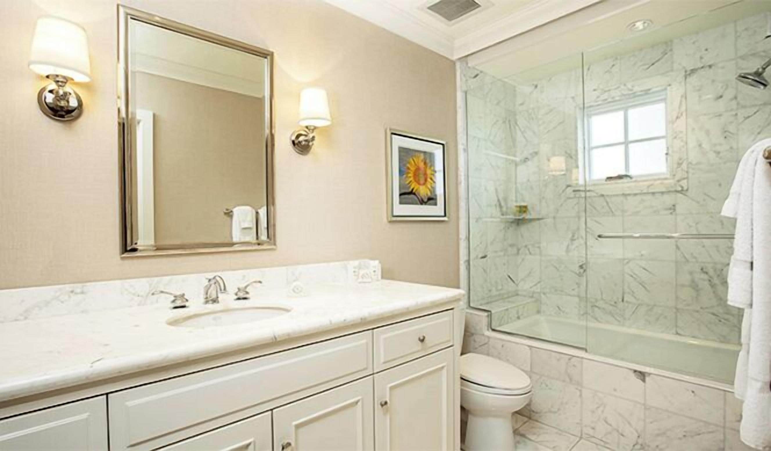 A bathroom with a marble sink, a large mirror, a framed picture, and a glass-enclosed shower.