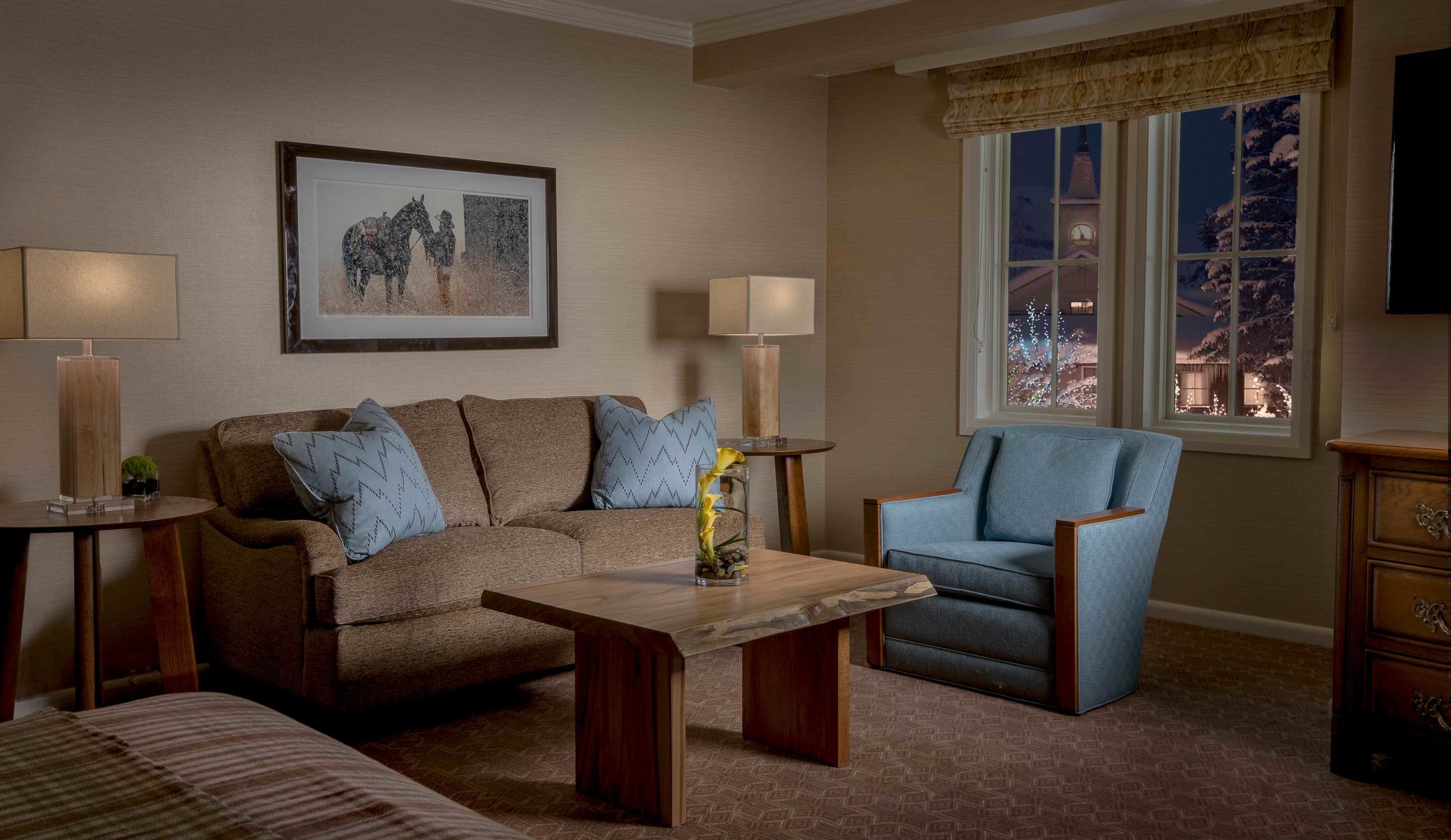 A cozy living room with a sofa, armchair, and coffee table, a framed picture on the wall, and a window with a view of a snowy landscape.