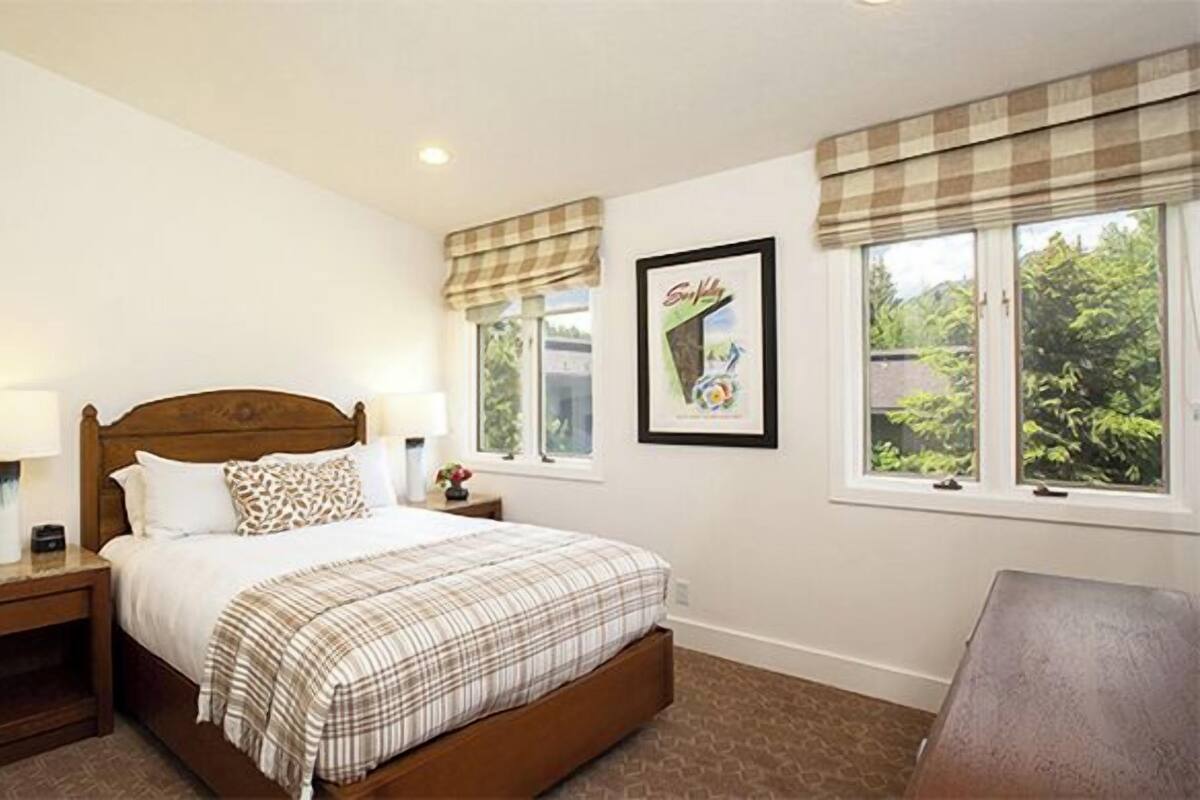 A bedroom with a bed, nightstands, a lamp, a framed picture, and a window with curtains.