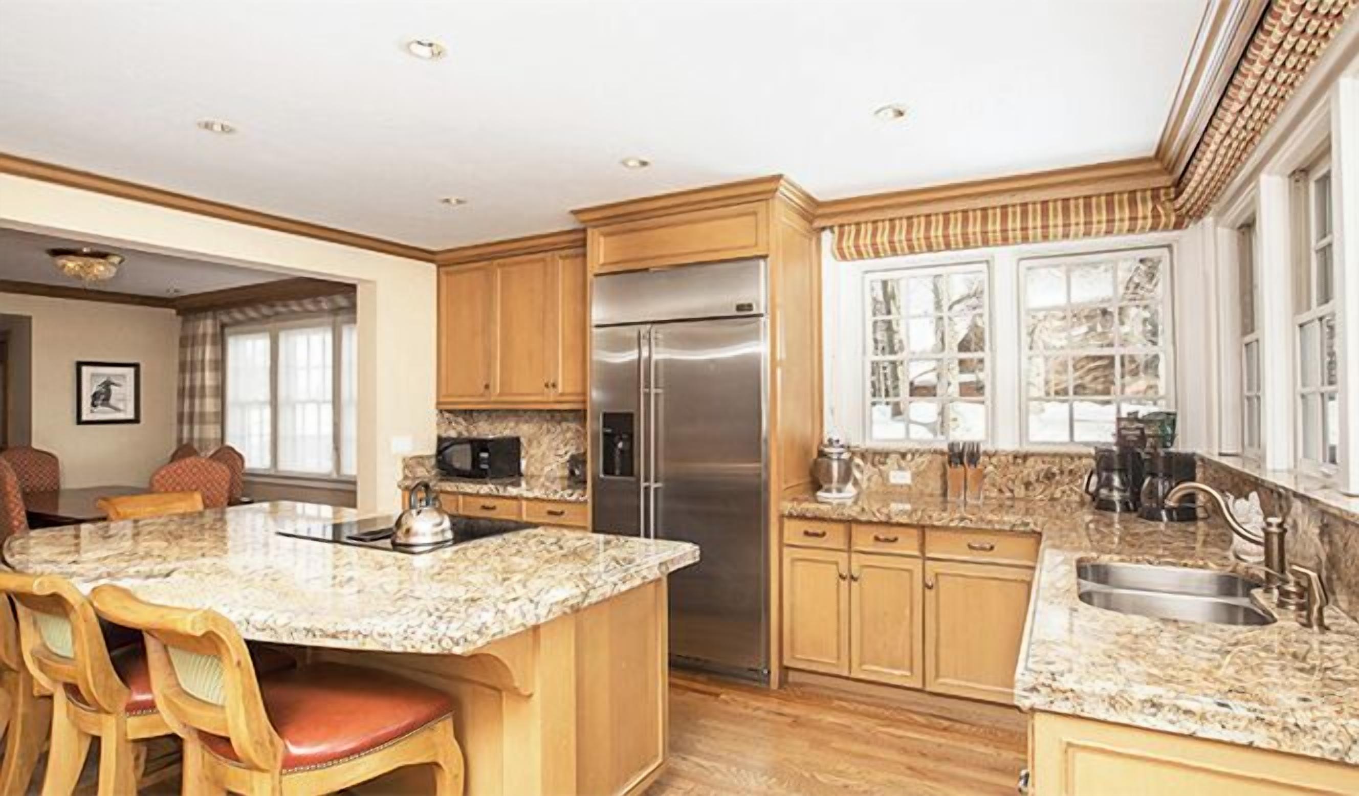 Una cocina amplia con encimeras de granito, gabinetes de madera, un refrigerador de acero inoxidable y una isla grande con taburetes de bar.