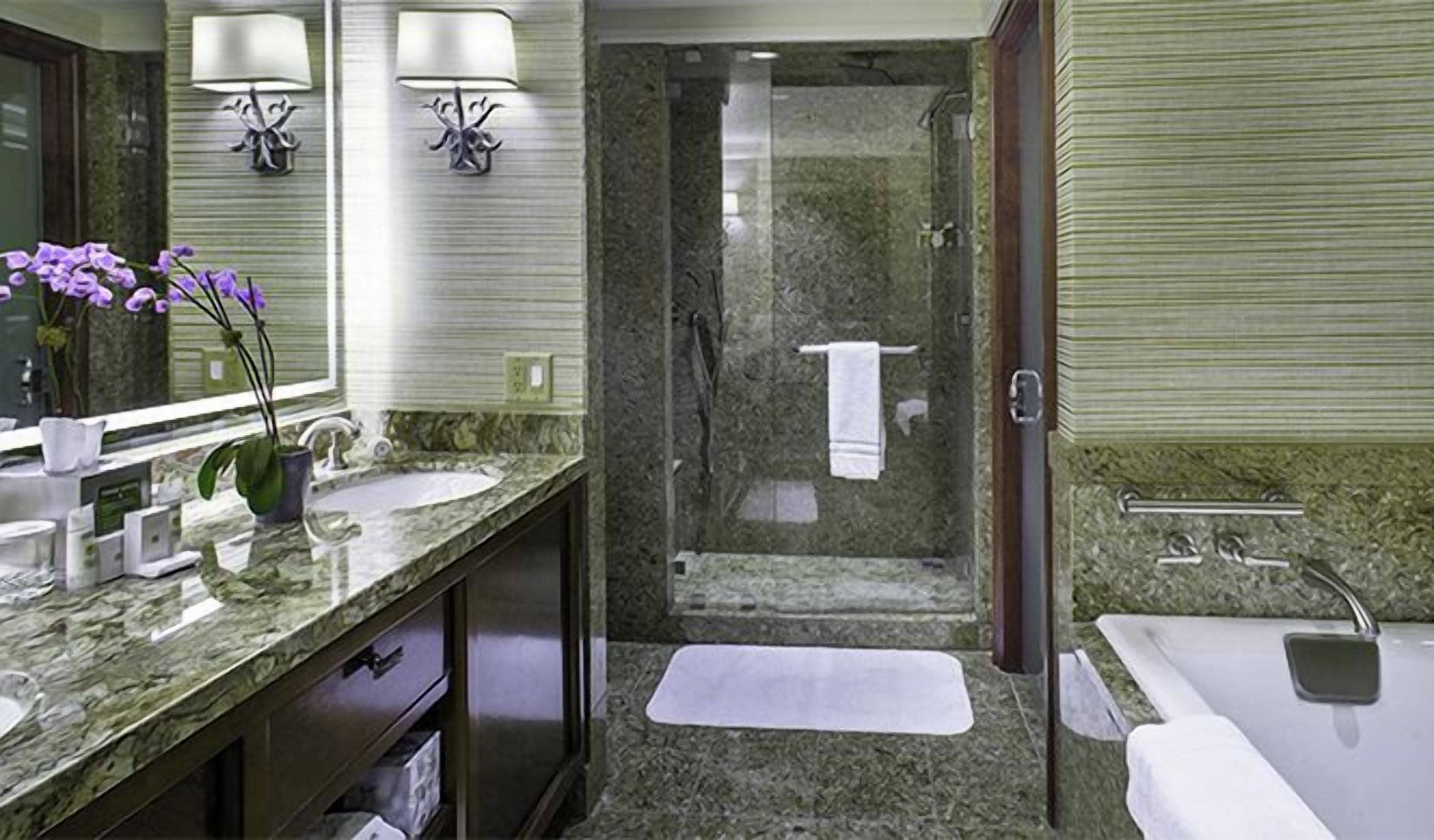 Uma casa de banho moderna com bancada de granito, um espelho grande, duas luzes na parede, chuveiro e banheira.